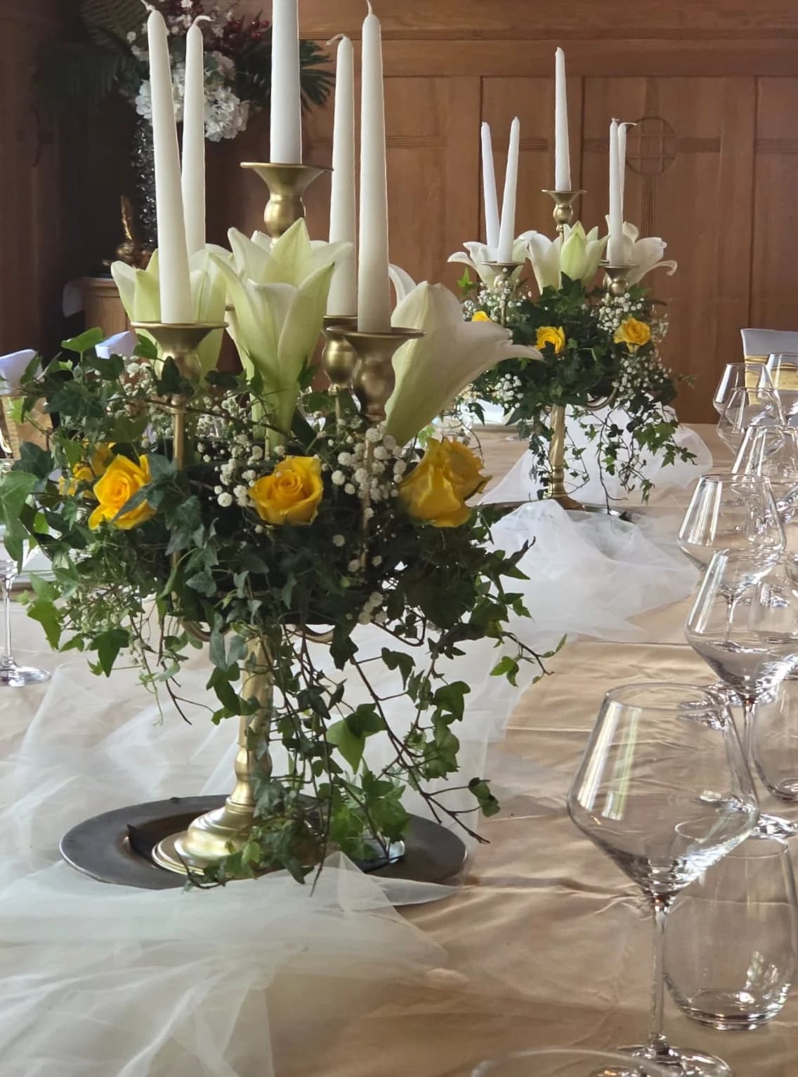 Goldene Kandelaber mit weißen Kerzen, weißen Lilien, gelben Rosen und Efeu — Tischdeko-Detail im Goldoni-Saal.