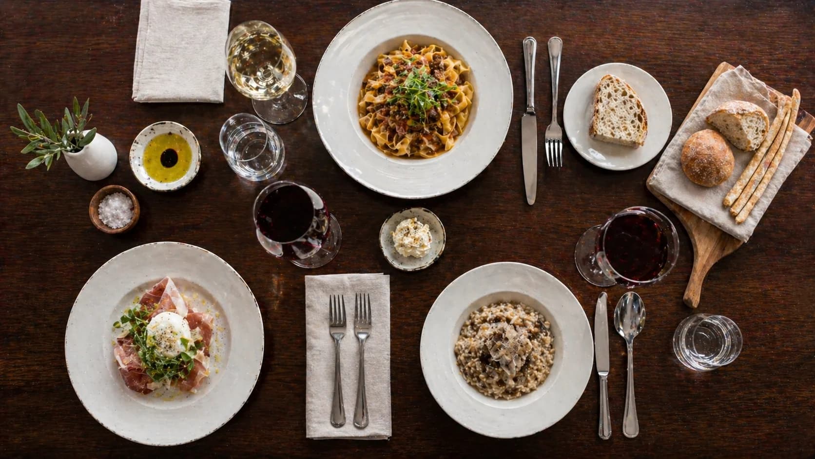 Gedeckter Tisch von oben: Pappardelle, Risotto ai funghi e tartufo, Burrata e prosciutto, Weingläser und Brot — wöchentliche Empfehlungen im Ristorante Goldoni