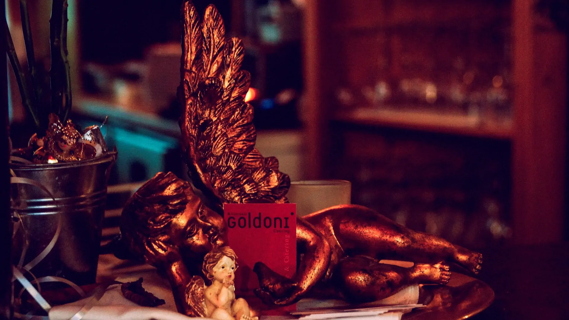 Goldoni Visitenkarte vor goldener Engelsfigur auf einem Tisch